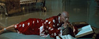 Movie still from “The King and I” (1956), directed by Walter Lang – A bald man in a red and white robe is laying on the floor; Medium shot, High angle