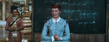 Movie still from “The King and I” (1956), directed by Walter Lang – A woman in a blue dress standing in front of a chalkboard; Medium shot, High angle
