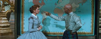 Movie still from “The King and I” (1956), directed by Walter Lang – A man and a woman are pointing at each other in front of a world map; Medium shot, Over the shoulder angle