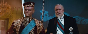 Movie still from “The King and I” (1956), directed by Walter Lang – A man and a man in a suit and tie standing next to each other in front of a blue wall; Medium shot, Low angle