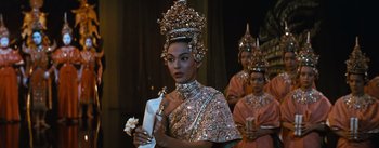 Movie still from “The King and I” (1956), directed by Walter Lang – A woman in a costume is holding a flower; Medium shot, Over the shoulder angle