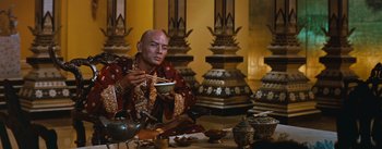 Movie still from “The King and I” (1956), directed by Walter Lang – A bald man in oriental garb eats a bowl of food; Medium shot, Over the shoulder angle