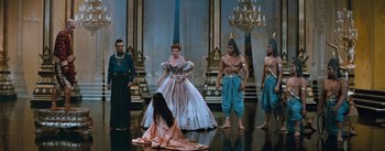 Movie still from “The King and I” (1956), directed by Walter Lang – A group of people standing around a woman in a ball gown; Wide shot, High angle
