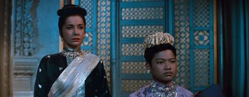 Movie still from “The King and I” (1956), directed by Walter Lang – Two women in traditional dress standing next to each other in front of a blue wall; Medium shot, Low angle