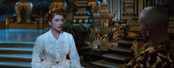 Movie still from “The King and I” (1956), directed by Walter Lang – A woman in a white dress sitting in front of a statue; Medium shot, Over the shoulder angle