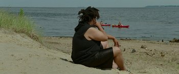 Movie still from “The King of Staten Island” (2020), directed by Judd Apatow – A woman sitting on the beach looking out at the ocean; Medium shot, High angle