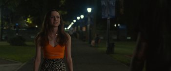 Movie still from “The King of Staten Island” (2020), directed by Judd Apatow – A woman in an orange and black top standing on a sidewalk at night; Medium shot, Over the shoulder angle