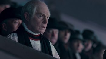 Movie still from “The King's Speech” (2010), directed by Tom Hooper – An old man wearing a black and red scarf; Close Up shot, Over the shoulder angle