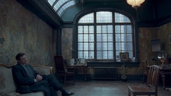 Movie still from “The King's Speech” (2010), directed by Tom Hooper – A man sitting on a couch in a room with a large window; Wide shot, High angle