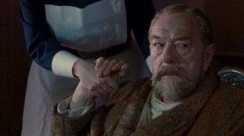 Movie still from “The King's Speech” (2010), directed by Tom Hooper – An older man sitting down with a hand on his chest; Close Up shot, Over the shoulder angle