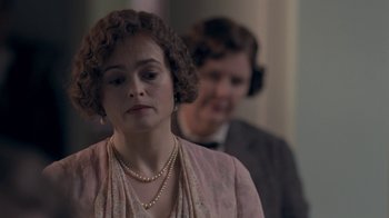 Movie still from “The King's Speech” (2010), directed by Tom Hooper – A woman in a pink dress and a man in a brown suit stand in the background; Close Up shot, Over the shoulder angle