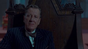 Movie still from “The King's Speech” (2010), directed by Tom Hooper – An older man wearing a suit and bow tie in front of a wooden wall; Close Up shot, Low angle