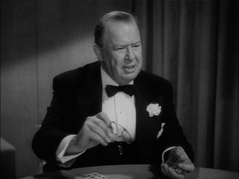 Movie still from “The Lady Eve” (1941), directed by Preston Sturges – An older man sitting at a table holding a pair of playing cards; Close Up shot, High angle