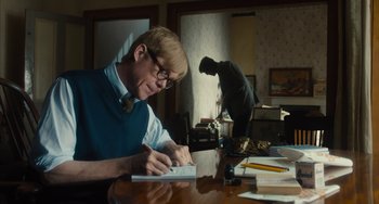 Movie still from “The Lady in the Van” (2015), directed by Nicholas Hytner – A man sitting at a table writing on a piece of paper; Medium shot, Low angle