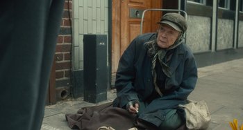 Movie still from “The Lady in the Van” (2015), directed by Nicholas Hytner – An older woman sitting on the ground in front of a brick building; Medium shot, Over the shoulder angle