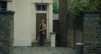 Movie still from “The Lady in the Van” (2015), directed by Nicholas Hytner – An older man standing in front of a door way; Wide shot, Low angle