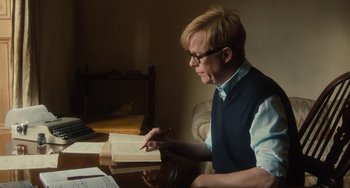 Movie still from “The Lady in the Van” (2015), directed by Nicholas Hytner – A man sitting at a table writing on a book; Medium shot, Over the shoulder angle