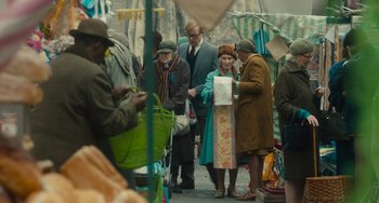 Movie still from “The Lady in the Van” (2015), directed by Nicholas Hytner – A group of people standing around a market area; Medium shot, Over the shoulder angle