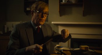Movie still from “The Lady in the Van” (2015), directed by Nicholas Hytner – A man in a suit and tie holding a knife and a cup; Medium shot, Low angle