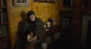 Movie still from “The Lady in the Van” (2015), directed by Nicholas Hytner – An older woman sitting in a chair holding a book; Medium shot, High angle