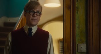 Movie still from “The Lady in the Van” (2015), directed by Nicholas Hytner – A man wearing a red vest standing next to a wall; Medium shot, Over the shoulder angle