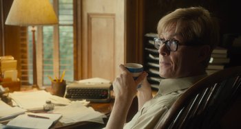 Movie still from “The Lady in the Van” (2015), directed by Nicholas Hytner – A man sitting at a desk holding a coffee cup; Medium shot, Over the shoulder angle