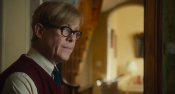 Movie still from “The Lady in the Van” (2015), directed by Nicholas Hytner – A man in a red sweater wearing glasses and a blue tie; Close Up shot, Over the shoulder angle