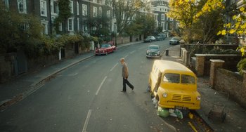 Movie still from “The Lady in the Van” (2015), directed by Nicholas Hytner – A man walking down a street past parked cars; Extreme Wide shot, High angle