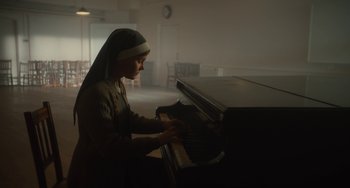 Movie still from “The Lady in the Van” (2015), directed by Nicholas Hytner – A nun is playing the piano in the dark; Medium shot, High angle