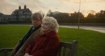 Movie still from “The Lady in the Van” (2015), directed by Nicholas Hytner – An older man and woman sitting on a park bench; Medium shot, Over the shoulder angle