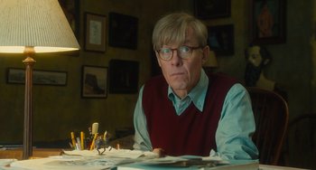 Movie still from “The Lady in the Van” (2015), directed by Nicholas Hytner – An older man sitting at a table in front of papers; Medium shot, Low angle