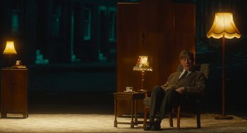 Movie still from “The Lady in the Van” (2015), directed by Nicholas Hytner – A man sitting in a chair in front of a lamp; Wide shot, Over the shoulder angle