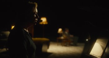 Movie still from “The Lady in the Van” (2015), directed by Nicholas Hytner – A woman is smoking a cigarette in a dimly - lit room; Medium shot, Over the shoulder angle