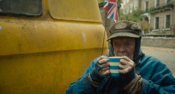 Movie still from “The Lady in the Van” (2015), directed by Nicholas Hytner – An older man holding a cup in his hands; Medium shot, High angle