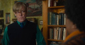 Movie still from “The Lady in the Van” (2015), directed by Nicholas Hytner – An older man standing in front of a book shelf; Medium shot, Over the shoulder angle