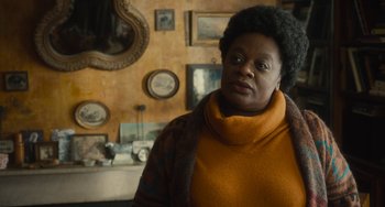 Movie still from “The Lady in the Van” (2015), directed by Nicholas Hytner – An older black woman standing in front of a wall of pictures; Close Up shot, Over the shoulder angle