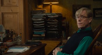 Movie still from “The Lady in the Van” (2015), directed by Nicholas Hytner – An older woman sitting at a desk in front of stacks of papers; Medium shot, Over the shoulder angle