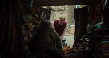 Movie still from “The Lady in the Van” (2015), directed by Nicholas Hytner – A man standing in front of a pile of clothes; Medium shot, Over the shoulder angle