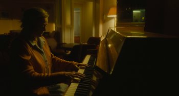Movie still from “The Lady in the Van” (2015), directed by Nicholas Hytner – A person playing the piano in a living room; Medium shot, High angle