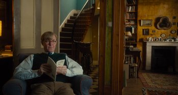 Movie still from “The Lady in the Van” (2015), directed by Nicholas Hytner – A man sitting in a chair reading a book; Medium shot, Low angle