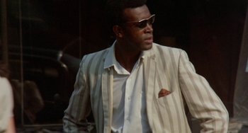 Movie still from “The Landlord” (1970), directed by Hal Ashby – A man in a suit and sunglasses is walking outside; Medium shot, Low angle