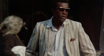 Movie still from “The Landlord” (1970), directed by Hal Ashby – A man wearing a suit and sunglasses walking down a street; Medium shot, Low angle