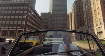 Movie still from “The Landlord” (1970), directed by Hal Ashby – A man driving a car down a street in a city; Wide shot, High angle