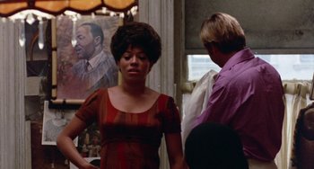 Movie still from “The Landlord” (1970), directed by Hal Ashby – A woman in a red dress standing next to a man in a purple shirt; Medium shot, Over the shoulder angle