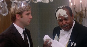 Movie still from “The Landlord” (1970), directed by Hal Ashby – Two men in suits are holding a tissue and one of them is shaving another man's head; Close Up shot, Over the shoulder angle