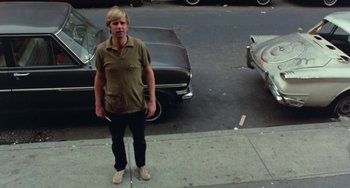 Movie still from “The Landlord” (1970), directed by Hal Ashby – A man standing on the side of the road next to cars; Wide shot, High angle