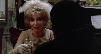 Movie still from “The Landlord” (1970), directed by Hal Ashby – An older woman sitting at a table with a glass of wine in front of her; Close Up shot, Over the shoulder angle