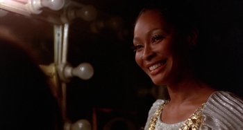 Movie still from “The Landlord” (1970), directed by Hal Ashby – A woman smiling for the camera in front of lights; Close Up shot, Over the shoulder angle