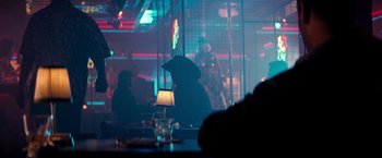 Movie still from “The Last Boy Scout” (1991), directed by Tony Scott – A person sitting at a table in a dark room; Wide shot, Over the shoulder angle