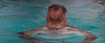 Movie still from “The Last Boy Scout” (1991), directed by Tony Scott – An older man swimming in a pool of water; Close Up shot, High angle